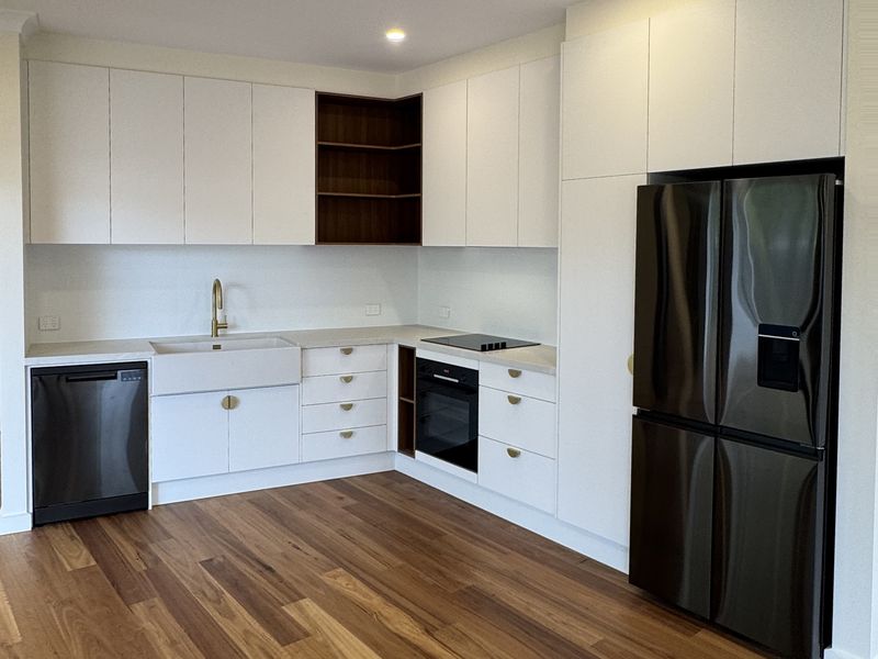 Kitchenette with white cabinetry and a black fridge, opening onto a wide timber floor