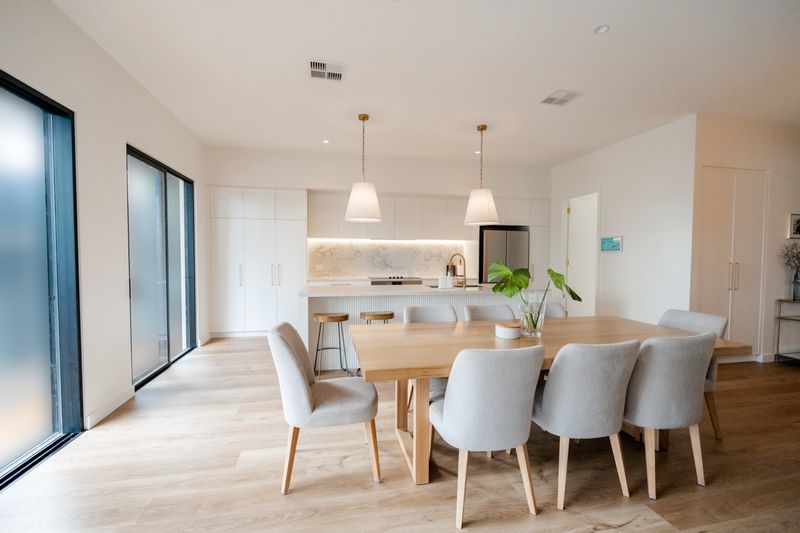 Dining table and chairs under pendant lights, with the kitchen beyond