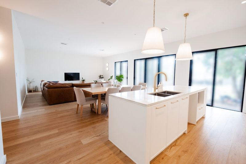 Open-plan kitchen island looking through to the living and dining area, with oak floors and black-framed sliding doors