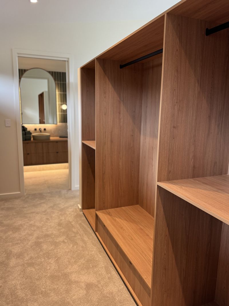 Walk-in robe in timber veneer joinery, with carpet and a view through to the lit bathroom